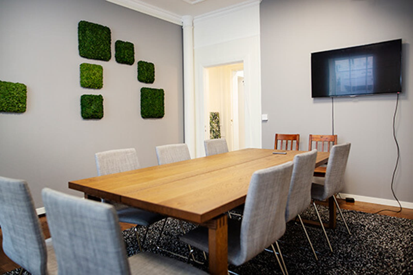 The Boardroom at The Ground — a long oak meeting table with grey fabric chairs, a TV screen on the wall, and moss art panels in soft green