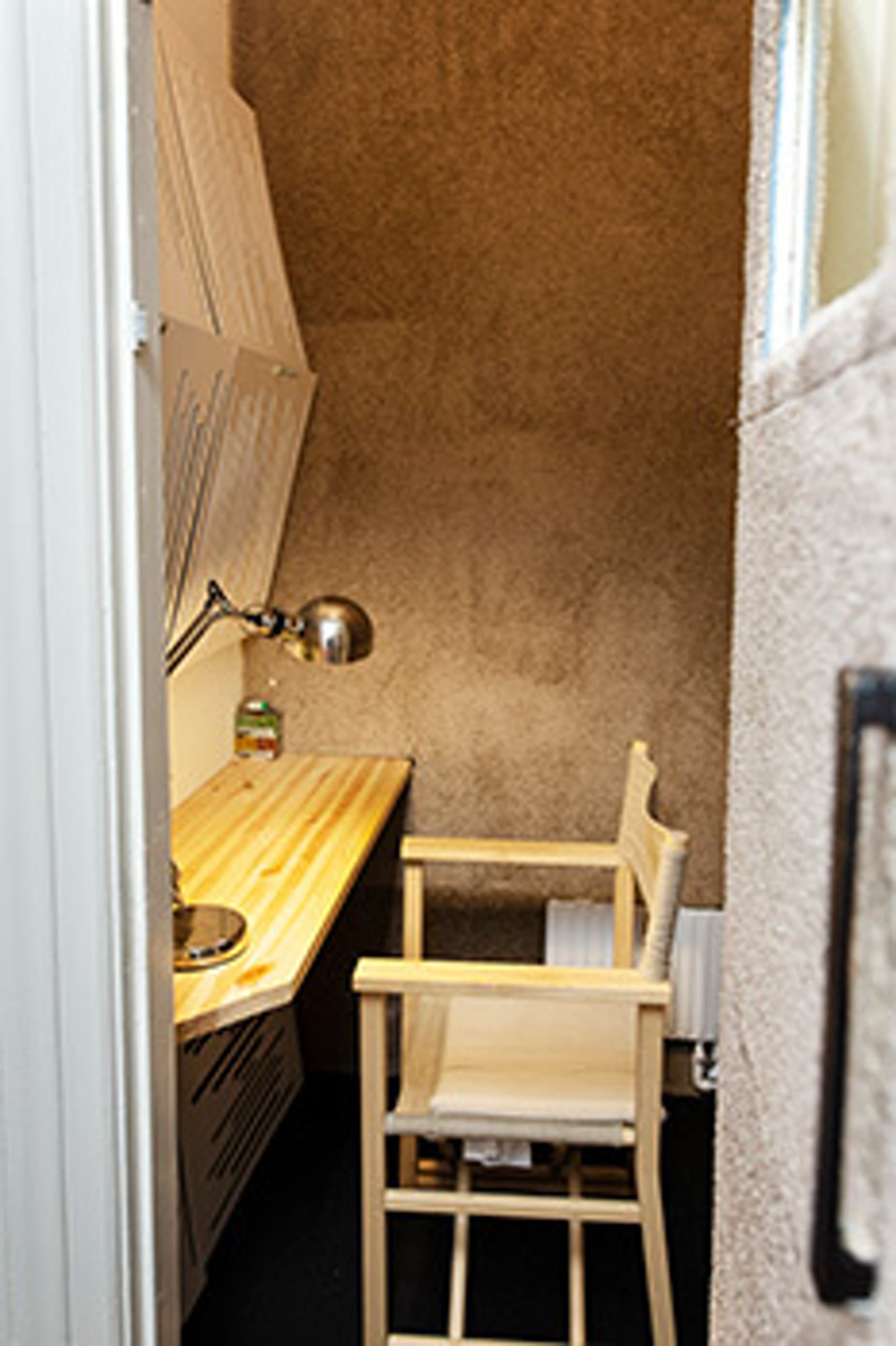 A private phone booth at The Ground with a small wooden desk, brass wall lamp, and woven chair — designed for one-to-one video meetings